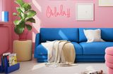 Wohnzimmer mit rosa Wänden und royalblauem Sofa und einem gelben Pouf