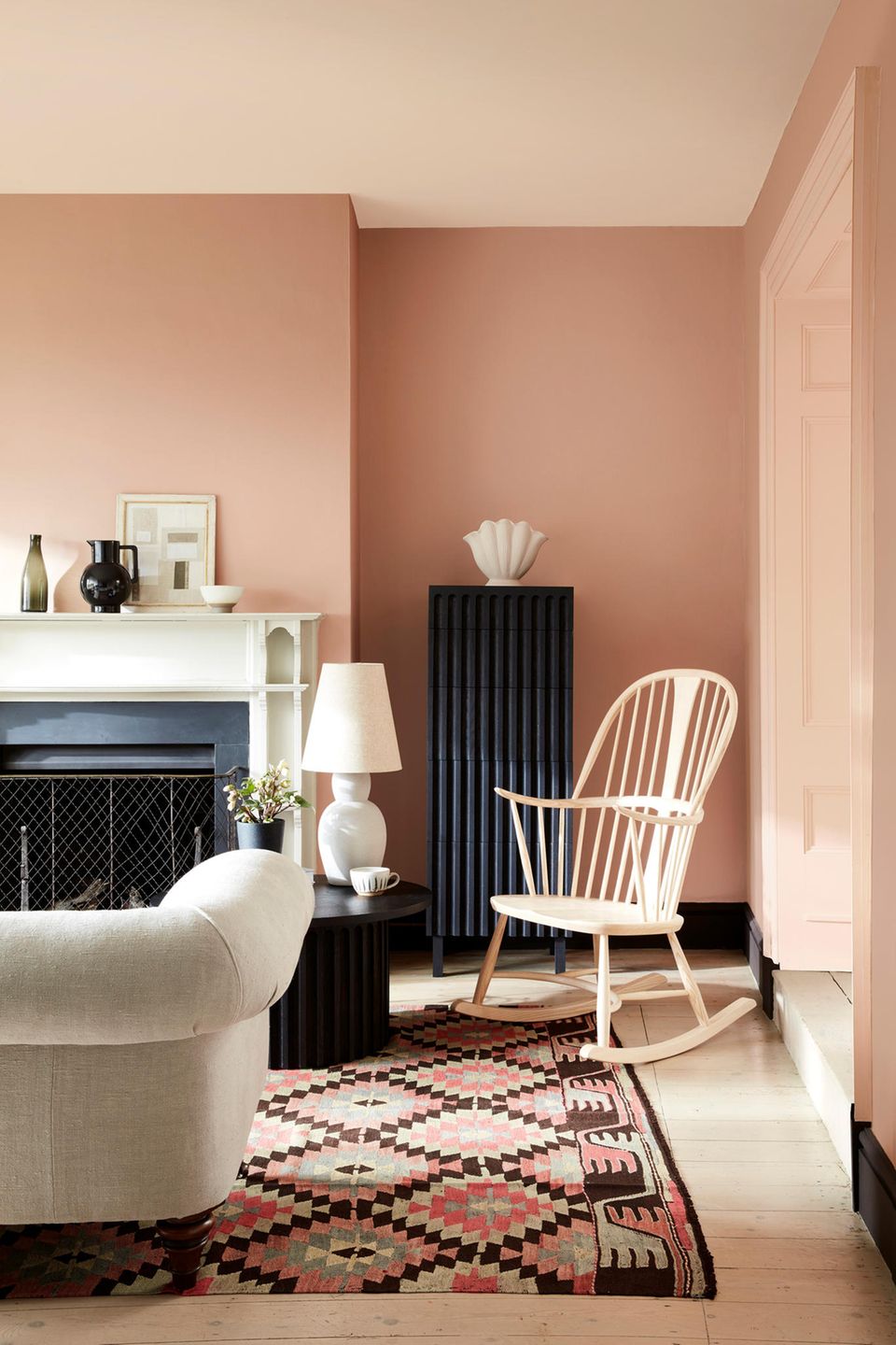 Wohnzimmer mit rosefarbener Wand hellen Möbeln und schwarzen Wohnelementen wie Kamin und Heizung