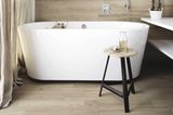 Badezimmer mit Fliesen in Holzoptik und einer freistehenden Badewanne mit Holzhocker