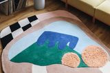 Designteppich in Rosa, Blau und Petrol vor gelbem Sofa auf hellem Holzfußboden an einem hellen Fenster