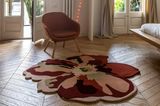 Teppich in Blütenform auf Holzdielen vor einem rosafarbenen Sessel und Fensterfront