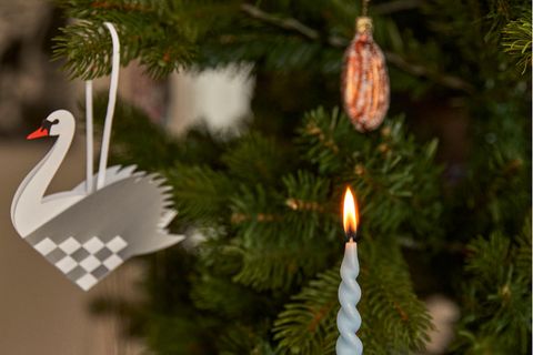 Eine gedrehte Kerze und ein Papierschwan als Weihnachtsbaumdeko an einem Tannenbaum