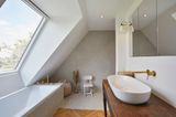 Badezimmer mit Badewanne unter einer Dachschräge mit großem Dachfenster und einem Waschtisch gegenüber.