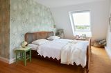 Schlafzimmer mit grün-geblümter Tapete, grünem Nachttisch und einem braunen Bett