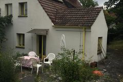Unsanierter Einfamilienhaus-Altbau mit einer Steinterrasse und weißen Plastikmöbeln im Vordergrund