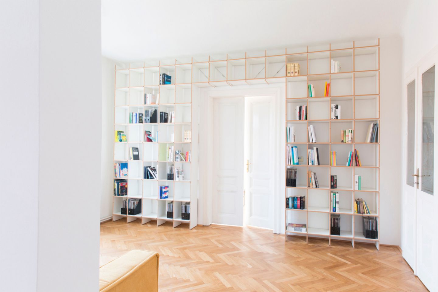Großer, heller Raum mit wandfüllendem Bücherregal mit Türüberbau