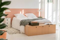 Helles Schlafzimmer mit halbhoch gestrichener Wand in rosa und Holzkommode am Bettende