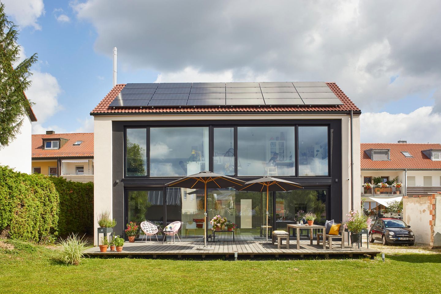 Holzterrasse und Gartenseite eines sanierten Hauses mit verglaster Fassade und Photovoltaikanlage auf dem Dach
