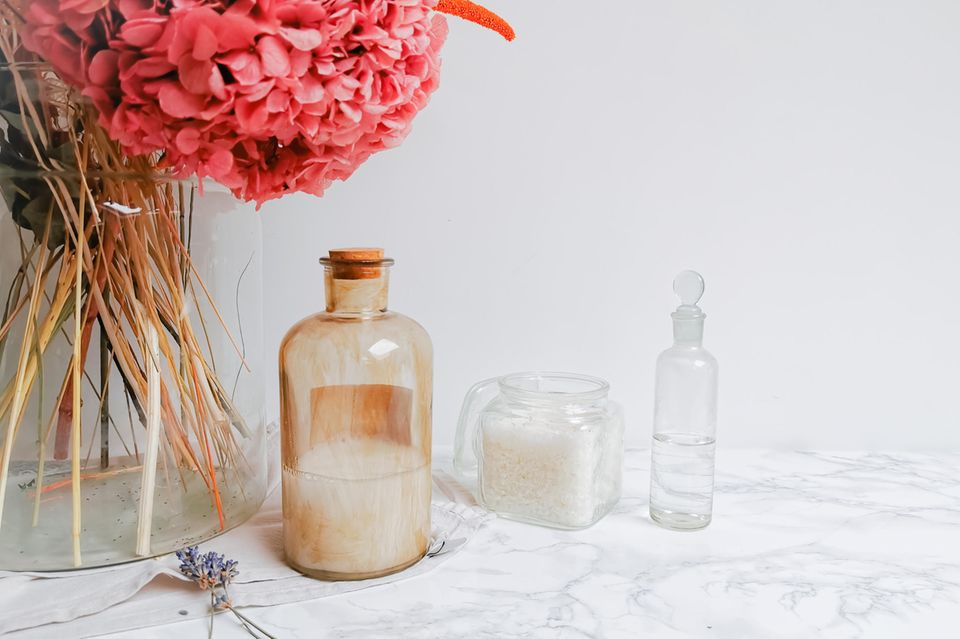 Glasflaschen und Kannen vor weißem Hintergrund mit einer pinken Blüte