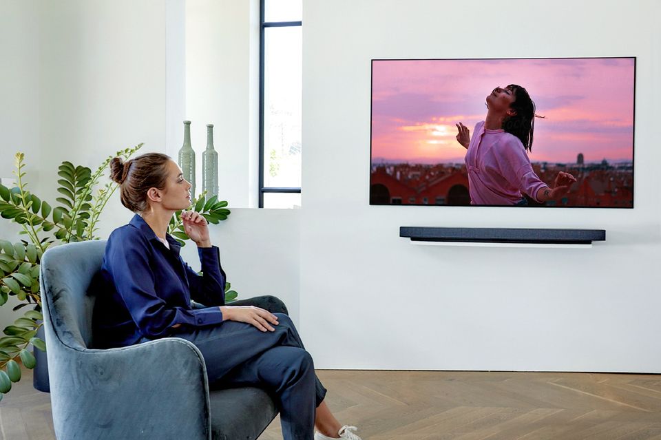 Frau im Sessel guckt auf einen LG-Fernseher an der Wand