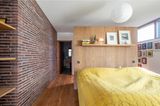 Bett mit gelbem Überwurf im Schlafzimmer mit Raumteiler aus Holz