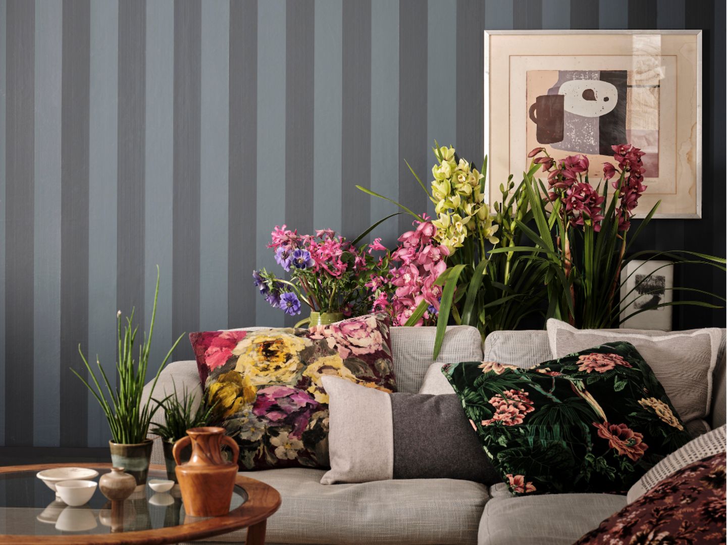 Sofa mit vielen Kissen vor üppigen Blumensträußen und blau-grau gestreifter Wand