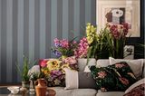 Sofa mit vielen Kissen vor üppigen Blumensträußen und blau-grau gestreifter Wand