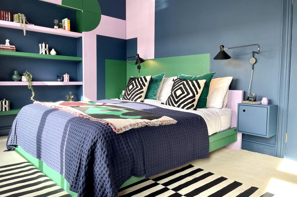 Schlafzimmer in Rosa, Grün und Blau mit Bett, Kissen, Regal und Nachtschränken