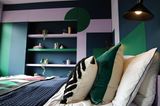 Kissen im Boho-Stil auf einem Bett vor einem Wandregal in Rosa, Grün und Blau