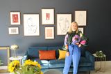 Farb-Queen Sophie Robinson vor einem blauen Sofa und einer dunklen Wand mit grafischen Bildern