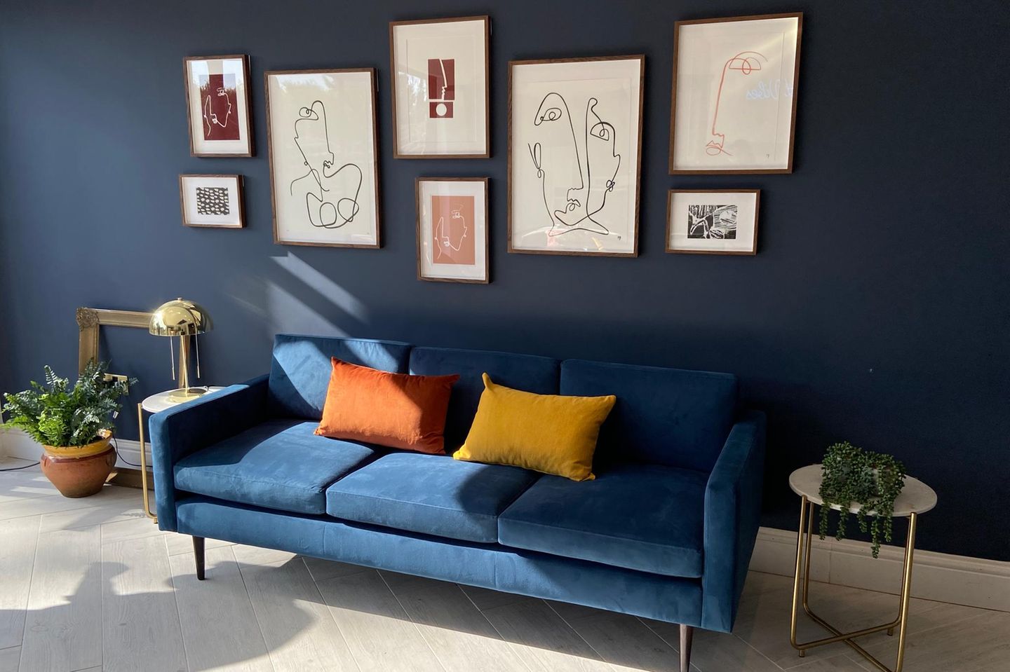 Blaues Sofa vor einer dunkelblauen Wand mit grafischen Bildern