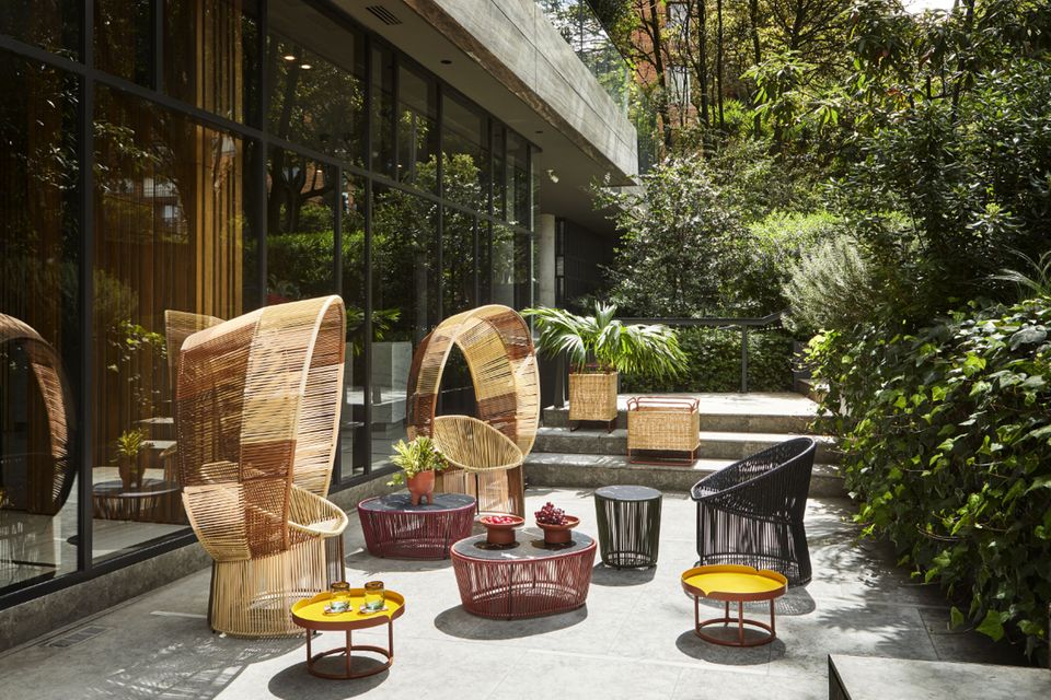 Zwei große, geflochtene Stühle mit bunten Beistelltischen auf sonniger Beton-Terrasse