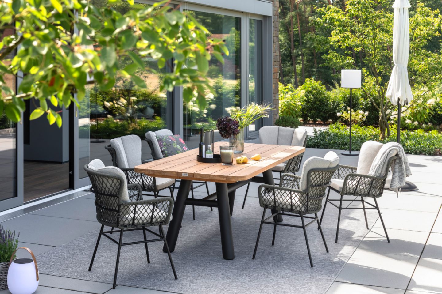 Gartenstühle aus dunklem Geflecht um einen Esstisch herum auf gefliester Terrasse