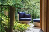 Sessel und Pouf aus Geflecht mit blauem Polster auf Balkon mit viel Grün im Hintergrund