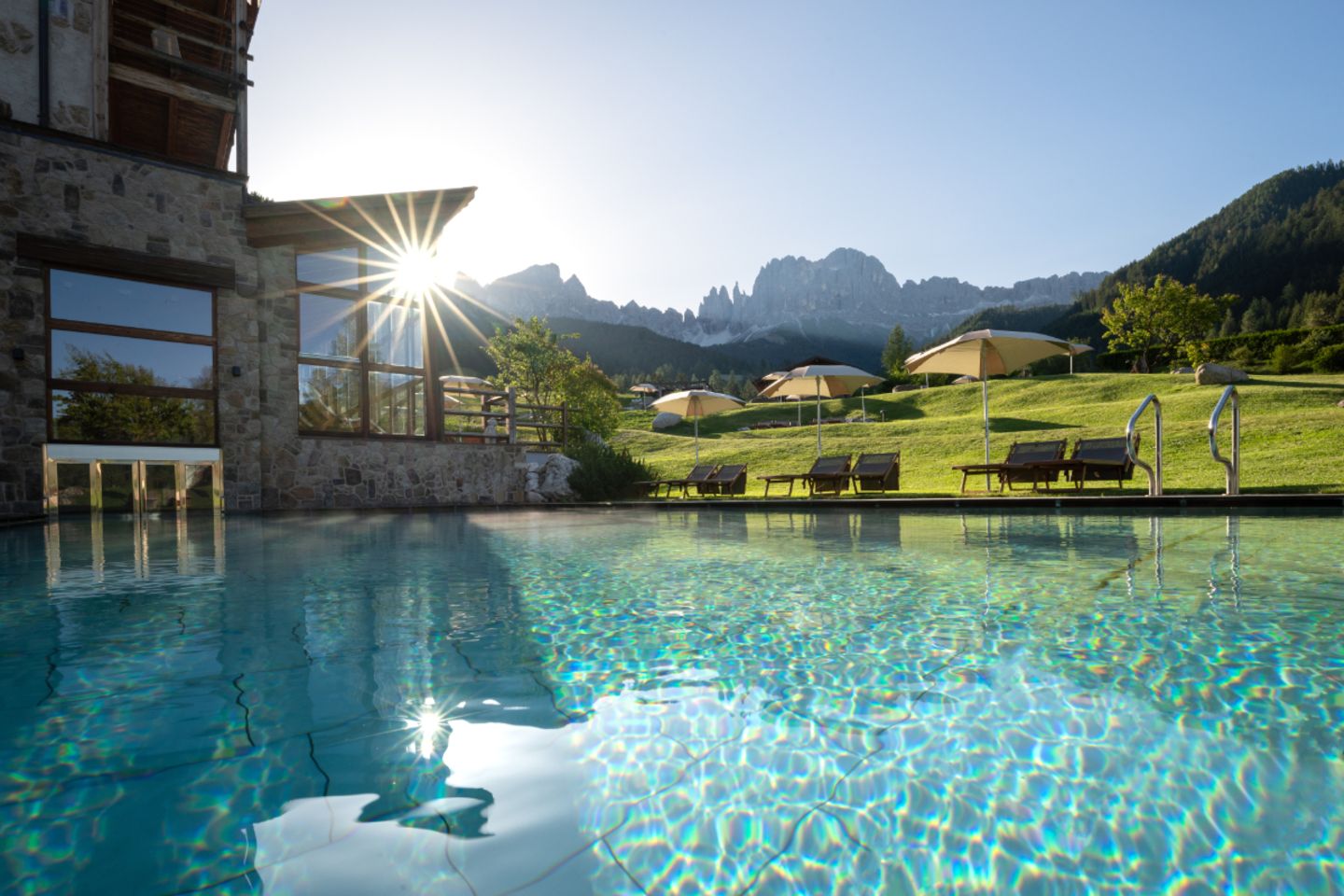 Hotel in den Bergen mit großem Pool und Sonne hinterm Haus