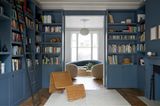 Bibliotheksraum mit blauen Bücherregalen, Flechtsessel und Blick ins Wohnzimmer