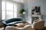 Blaues Sofa und zwei Bouclé-Sessel in Wohnzimmer mit großem Fenster und Kamin