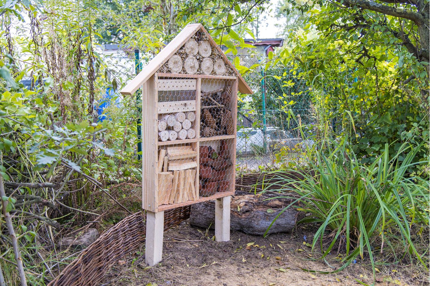 Selbstgebautes Insektenhotel aus Naturmaterialien vor einem Gartenzaun aus Maschendraht