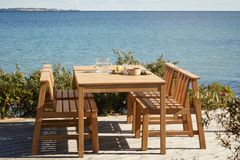 Tisch, Bank und Stühle aus dunklem Holz auf Holzterrasse am Meer