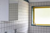 Weiß gekacheltes Badezimmer mit gelbem Fenster und blauer Wandfarbe
