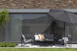 Dunkle Outdoor-Polstermöbel und schwarzer Sonnenschirm auf Steinterrasse vor verschattetem Haus