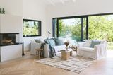 Wohnzimmer mit cremefarbenen Sofas und schwarz umrahmten Fenstern mit Blick ins Grüne