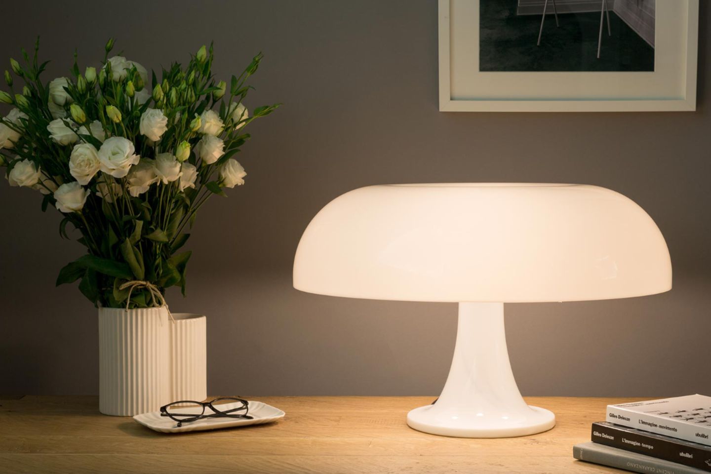 Weiße Kunststoff-Leuchte in ausladender Pilzform auf Nachttisch mit Blumenvase, Brille und Büchern