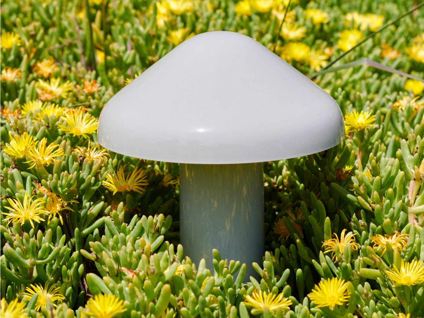 Graue Akkuleuchte in Pilzform mit glänzender Oberfläche inmitten von Pflanzen