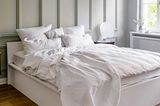 Weißes Doppelbett und Kassettenwand im Schlafzimmer und Hängeleuchte mit Schirmelementen aus Papier