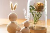 Zwei Osterhasen aus Holzkugeln neben einer Glasglocke