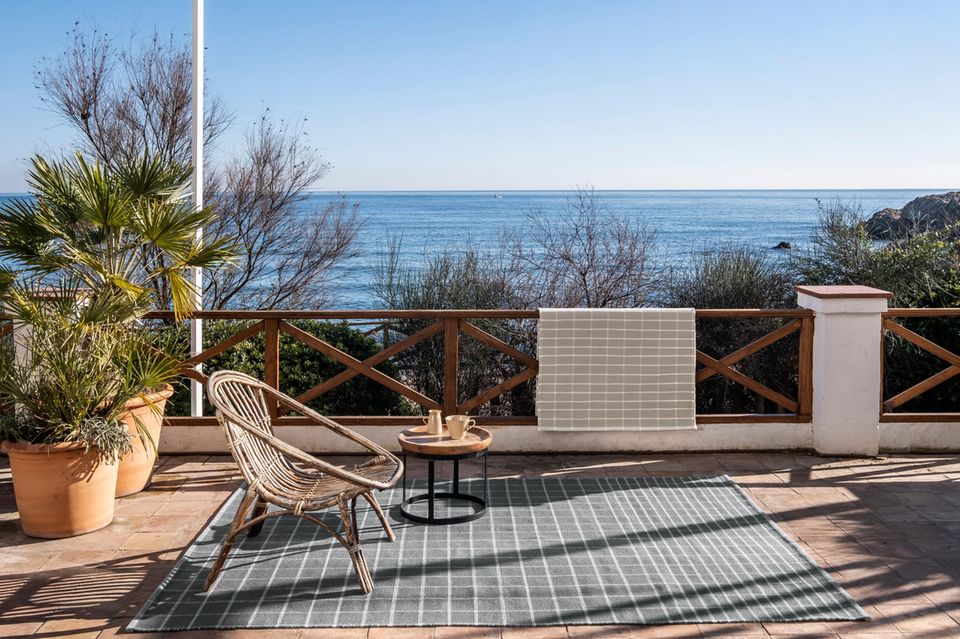 Karierter grauer Outdoorteppich auf einer Terrasse mit Meer im Hintergrund