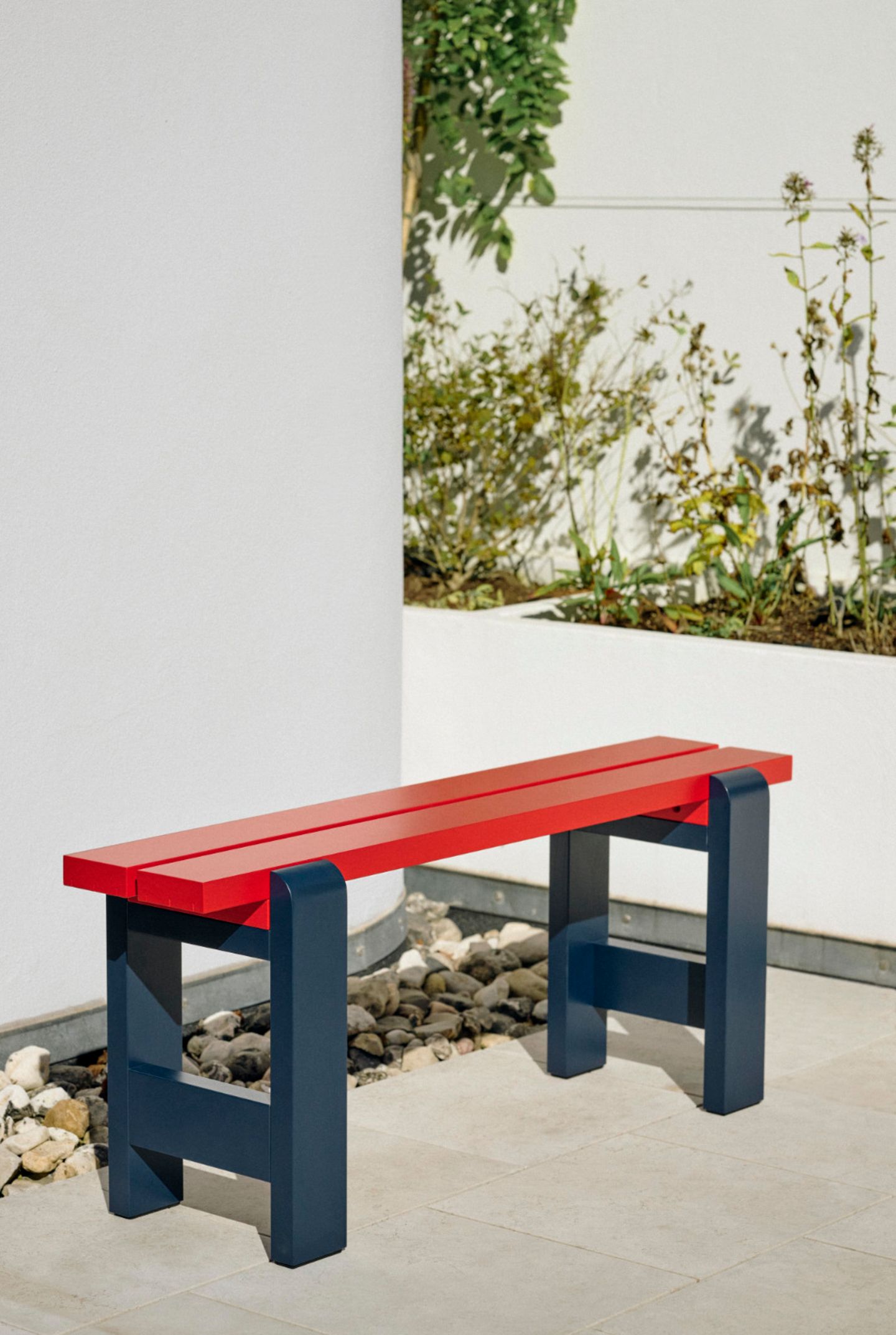 Kleine Sitzbank in den Farben Schwarz und Rot in einer Terrassenecke mit Grünpflanzen