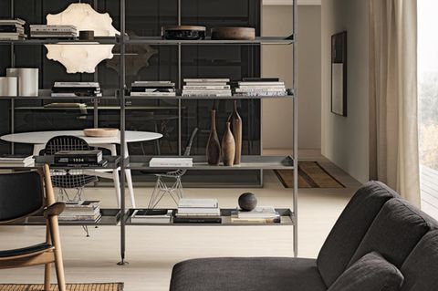 Ein bodenhohes Regal aus schwarzem Metall und Glas steht in einem Raum mit neutralen Decken- und Wandfarben