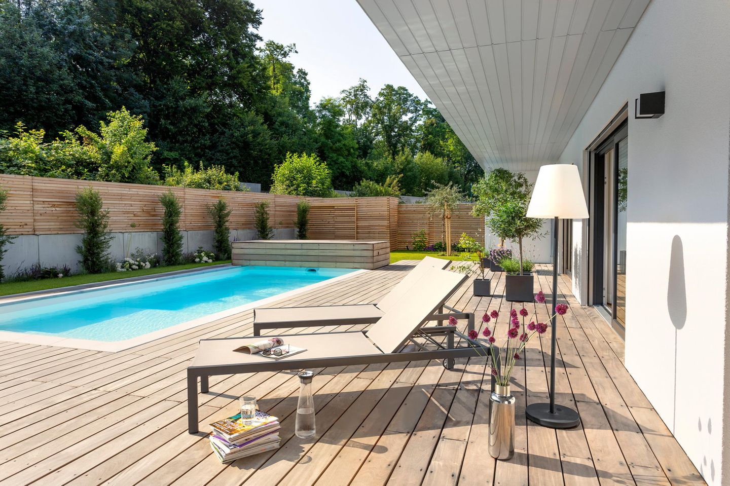 Auf einer Terrasse auf Holz stehen zwei Liegestühle vor einem Pool