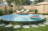 Ein runder Pool mit niedriger Hecke und Rasen vor einer kleinen Holzterrasse