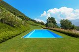 Ein großer blauer Pool auf einer grünen Rasenfläche mit Pflanzen und Bergen im Hintergrund