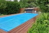 Eine blaue Poolabdeckung liegt auf einem Pool mit Holzdielen als Umrandung