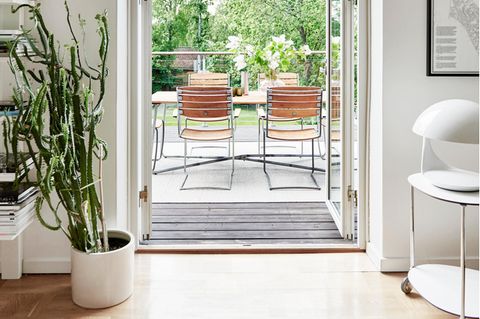 Blick durch eine Terrassentür mit Holz-Stahlrohrmöbeln und einer Zimmerpflanze links