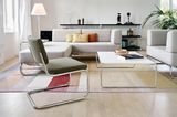 Freischwinger-Sessel vor einem grauen Sofa mit weißem Coutisch und schwarzem Regal an einer weißen Wand.
