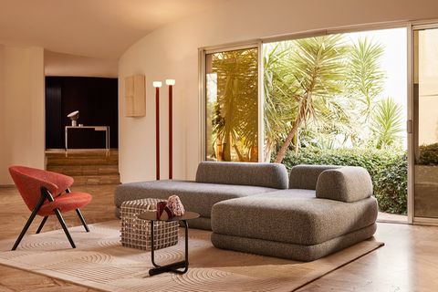 Graues Sofa vor einem bodentiefen Fenster mit Palmen im Hintergrund