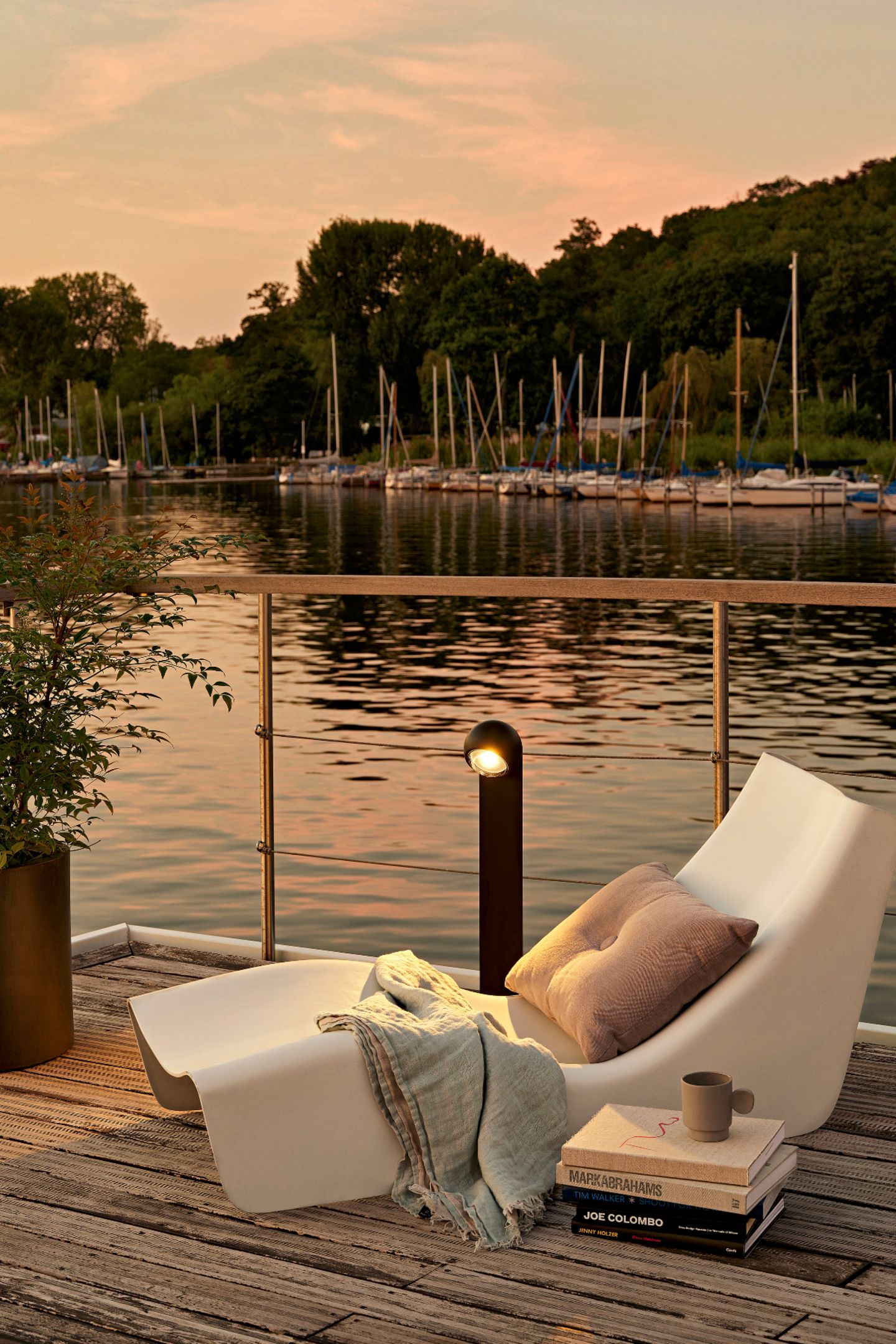Terrasse am Wasser mit weißer Liege und schwarzer Pollerleuchte in Abendstimmung
