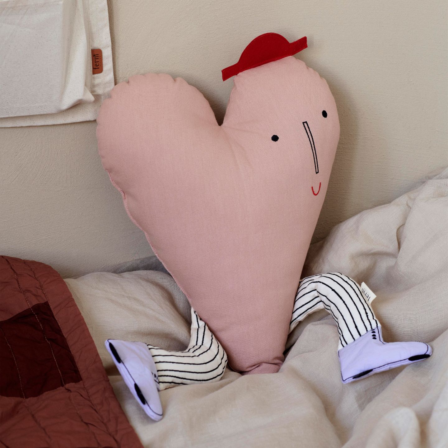 Herzförmiges, rosafarbenes Kissen mit Hut und Beinen auf Kinderbett