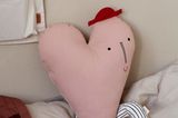 Herzförmiges, rosafarbenes Kissen mit Hut und Beinen auf Kinderbett