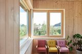 Holzwände mit bunten Sesseln und einem großen Fenster mit Blick ins Grüne.